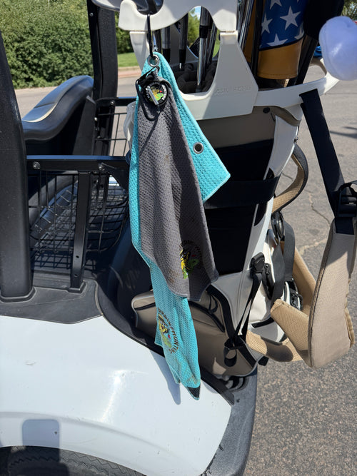 Happy Birdie Hunting golf towel set clipped to a golf cart via carabiner, showing the two-tone teal and grey waffle weave design in use on the course